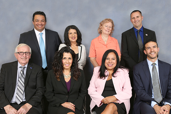 Eight board members in front of blue background.